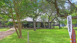 A house with a large tree in front and a signpost with numbers. - Darling Cottage with access to 2 Blanco River Parks! (Wimberley)