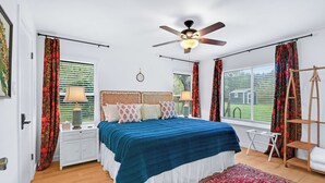 A bedroom with a bed, two bedside tables, a ceiling fan, a window with blinds, and a red patterned rug. - Darling Cottage with access to 2 Blanco River Parks! (Wimberley)