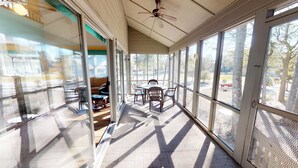 A sunroom with a ceiling fan, large windows, and a table with chairs.