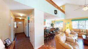 A spacious living area with a high ceiling, a kitchen with a bar, and a dining area with chairs.