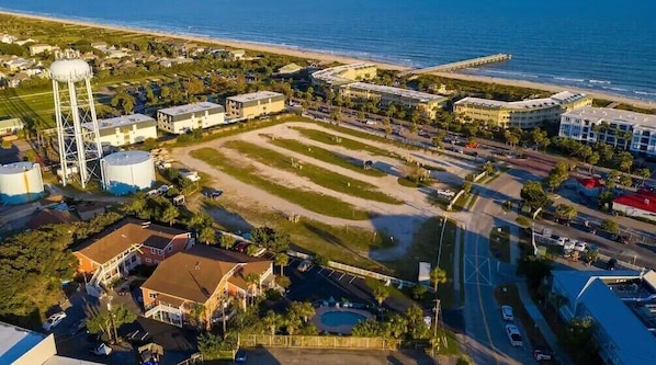 An aerial view of a coastal area with a large open field, buildings, and a water tower.