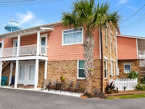 A two-story building with a brick facade, a balcony with white railings, and a palm tree in the front yard. - #101 Ocean Inn 2 Bedroom 1.5 Bath Modern Favorite (Isle of Palms)