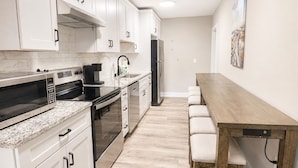 A modern kitchen with white cabinets, a stainless steel microwave, a coffee maker, and a wooden dining table with chairs.