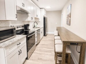 A modern kitchen with white cabinets, a stainless steel microwave, a coffee maker, and a wooden dining table with chairs.