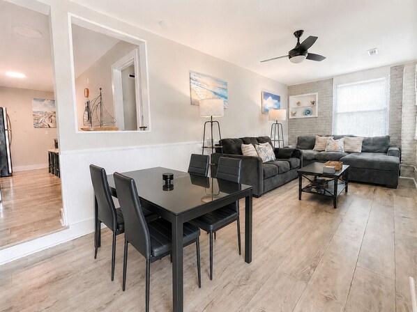 A modern living room with a dining area, a sectional sofa, and a ceiling fan. - #101 Ocean Inn 2 Bedroom 1.5 Bath Modern Favorite (Isle of Palms)