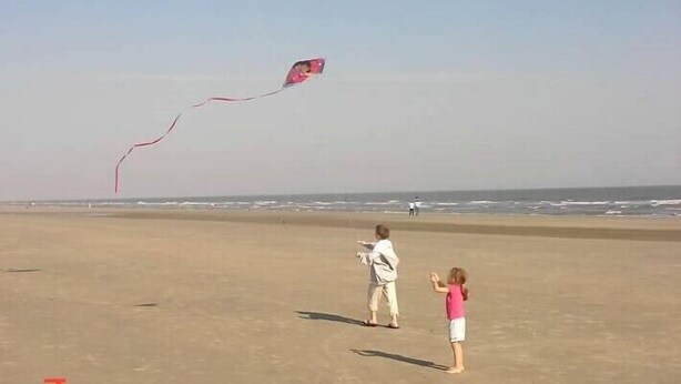 A beach with two people flying kites.