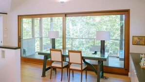 Ein Essbereich mit Tisch und Stühlen, große Fenster mit Blick auf Bäume und eine Lampe an jeder Seite des Tisches.