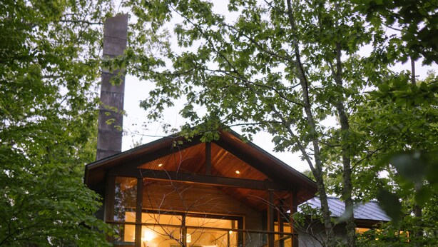 Ein modernes Haus mit einer großen Glasfassade, einer Holzdiele und einem Schornstein.