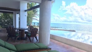 Eine Sitzecke mit Holzliegen und einem Tisch, mit Blick auf einen Strand und den Ozean.