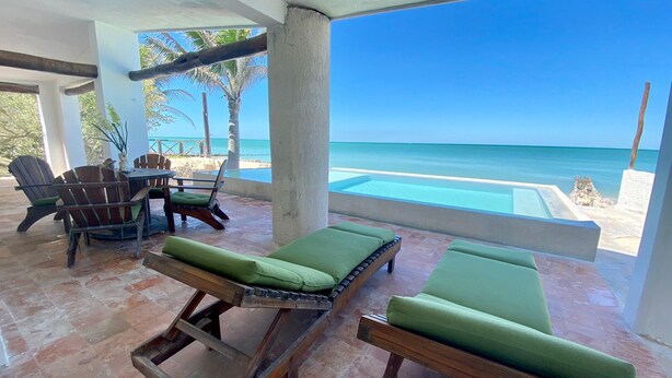 A poolside area with lounge chairs and a table, overlooking a beach and ocean. - La Tintinki, amaizing ocean view!! (Chelém)