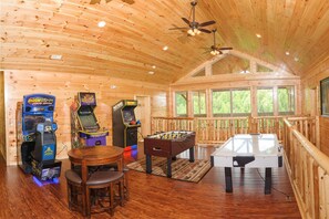 A wooden cabin interior with arcade games, a foosball table, and a dining area.