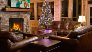 A cozy living room with a fireplace, leather couches, a Christmas tree, and a television on the wall. - Sycamore Mansion | 14 Suites | Arcade | Fire Pit | Amazing Views (Gatlinburg)