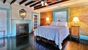 Une chambre à coucher avec un lit, une cheminée, un ventilateur de plafond et un mur en briques.
