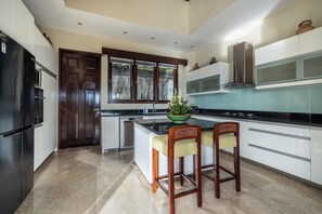 A modern kitchen with a central island, white cabinetry, and a dark wooden door. - Luxury Villa with private driver +welcome dinner, ocean views and amazing sunset (South Kuta)