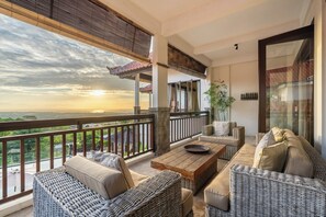 A balcony with wicker furniture, a wooden table, and a view of the landscape. - Luxury Villa with private driver +welcome dinner, ocean views and amazing sunset (South Kuta)