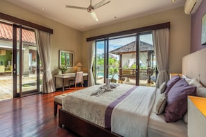 A spacious bedroom with a large bed, a desk, and a view of a pool and garden. - Luxury Villa with private driver +welcome dinner, ocean views and amazing sunset (South Kuta)