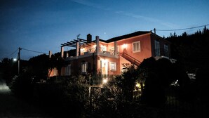 Une maison à deux étages avec un balcon, une antenne parabolique bien visible et un petit jardin.