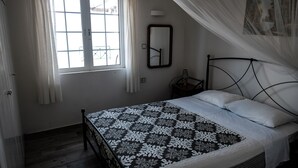 Une chambre à coucher avec un lit, une fenêtre avec des rideaux, une table de chevet avec une lampe et un miroir fixé au mur.