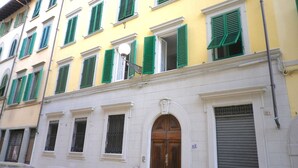 A multi-story building with green shutters on windows, a central arched doorway, and a closed shutter on the right. - Florence Historic Center | Private Courtyard | Walk to Everything, WIFI, AC (Firenze)
