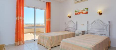 A hotel room with two beds, a balcony, a painting, and a lamp.