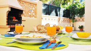 Une table dressée pour un petit-déjeuner en plein air, avec des assiettes remplies de nourriture, des verres de jus d’orange et un panier de pain.