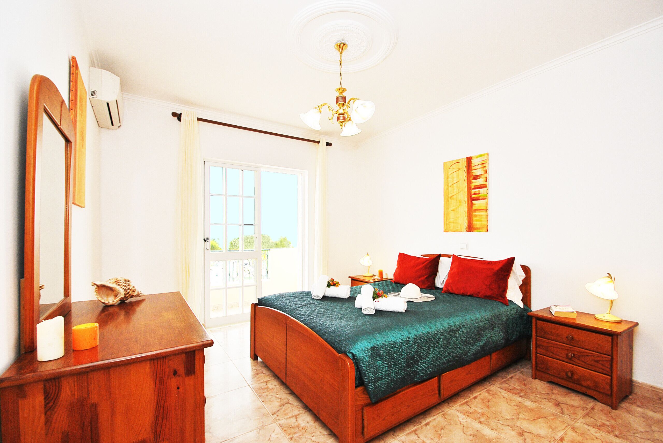 A bedroom with a wooden bed, a nightstand, a mirror, a window with curtains, and a ceiling light.