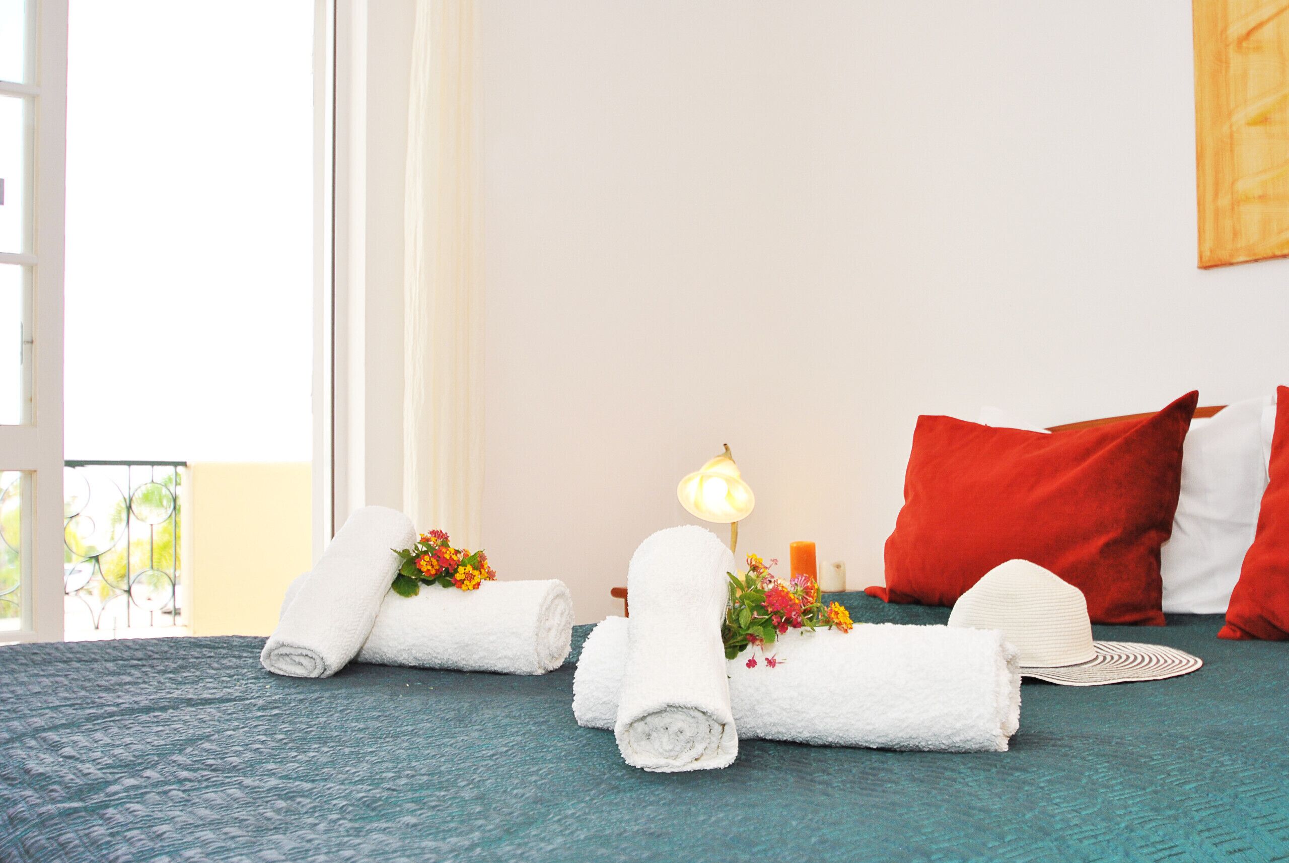 A neatly made bed with rolled white towels, a lamp, and a red pillow.