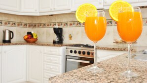 Deux verres de jus d’orange sont posés sur un comptoir de cuisine, devant des armoires blanches et un mur recouvert de carreaux.