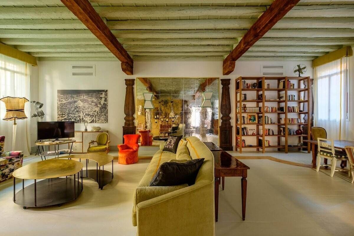 A spacious living room with a high ceiling, a television, a sofa, a coffee table, a bookshelf, and a dining area.