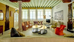 A spacious living room with a high ceiling, a central seating area with a sofa and chairs, a coffee table, and a television.