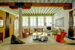 A spacious living room with a high ceiling, a central seating area with a sofa and chairs, a coffee table, and a television. - Ca' del Ramo D'oro (Venice)