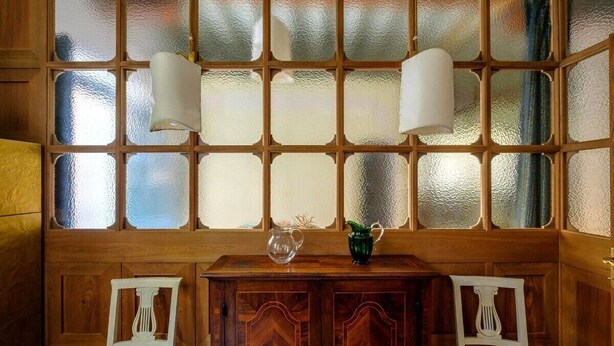 A room with a wooden cabinet, two white chairs, and a large window with frosted glass panels.