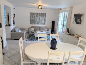 A dining area with a round table and chairs, a grey sofa, a coffee table, and a painting on the wall.