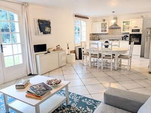 A modern kitchen with white cabinetry, a dining area with white chairs, and a small table with books and a bowl of snacks.