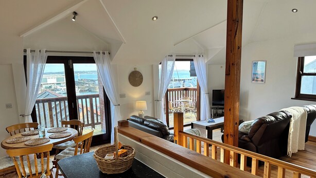 Ein geräumiger Wohnbereich mit Balkon und Blick auf eine Marina, einem Esstisch mit Platzsets sowie einer gemütlichen Sitzecke mit Ledersofa und Decke.