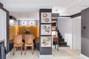 A dining area with a tufted yellow sofa, wooden chairs, and framed botanical prints on a wall.