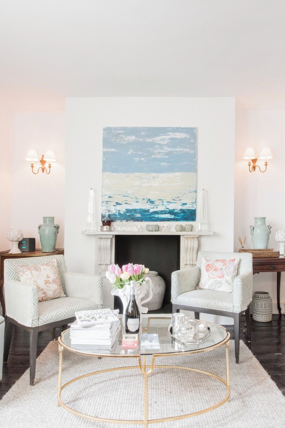 A living room with two armchairs, a coffee table, a fireplace, and a large abstract painting above the mantel.