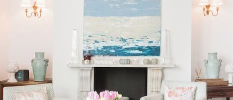 Un salon comprenant deux fauteuils, une table basse, une cheminée et un grand tableau abstrait accroché au-dessus du manteau de cheminée.