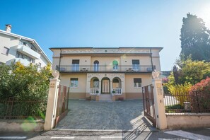 Un edificio de dos pisos con entrada porticada, un balcón y una pequeña escalera que conduce a la puerta principal.