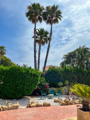A patio area with palm trees, green chairs, and a garden.