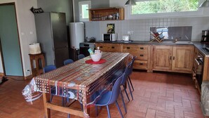 A kitchen with a tiled backsplash, a wooden table with chairs, a hanging light fixture, and a window with a view of greenery. - Small house by the sea (Plouha)