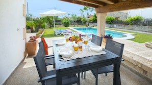 An outdoor patio with a table set for dining, a pool in the background, and a garden area. - VILLA  MARGARITA - 15 MIN WALK TO THE BEACH (Puerto Pollensa)