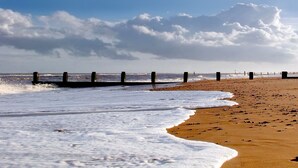 A beach with waves, a wooden jetty, and a clear sky.