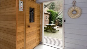A sauna with a control panel, a wooden door, and a view of a garden with a picnic table and a hanging ring.