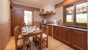 Een keuken met houten kastjes, een eettafel met stoelen, een magnetron en een raam met uitzicht.