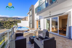 Une terrasse extérieure moderne, dotée d’une piscine, de chaises longues et d’un espace repas offrant une vue sur le paysage environnant.