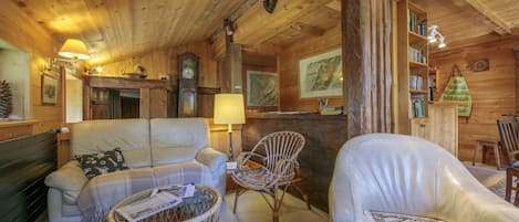 A cozy cabin interior with a sofa, chairs, a wicker basket, and a bookshelf.