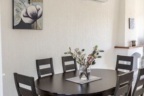 Ein runder Esstisch mit sechs Stühlen, eine Vase mit Blumen und ein Gemälde an der Wand.