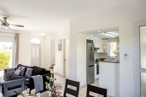 A modern living room with a sofa, chairs, and a dining table. There is a kitchen area with a refrigerator and cabinets.