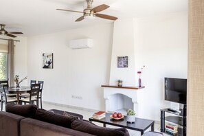 Un salon doté d’un ventilateur de plafond, d’une cheminée, d’un téléviseur et d’un coin repas avec des chaises et une table.
